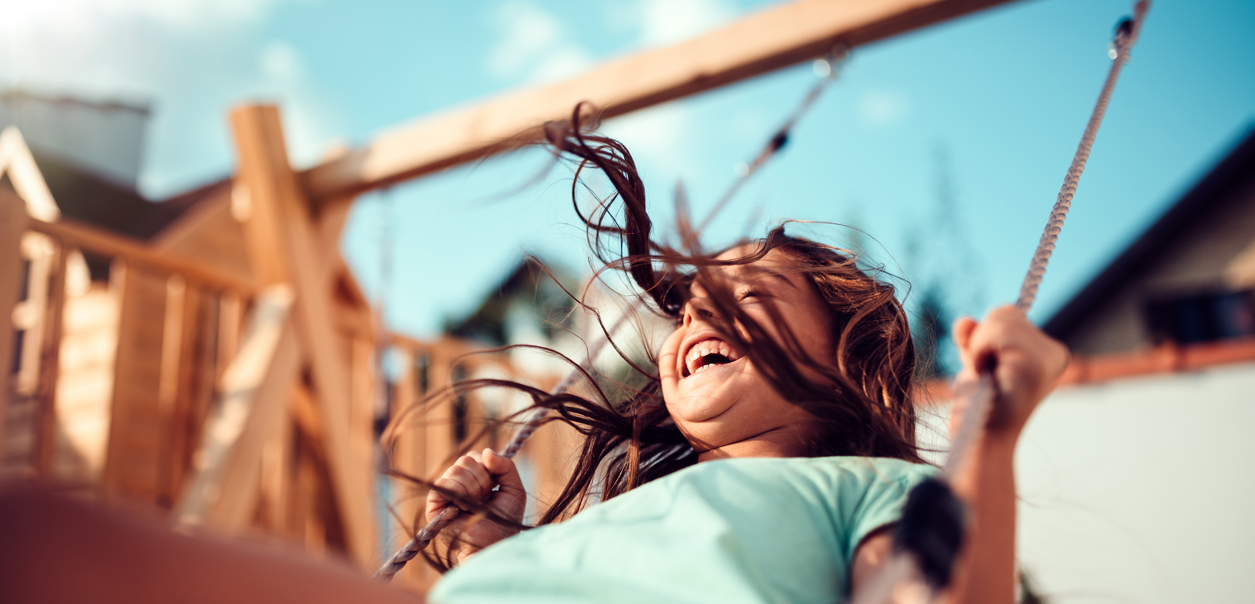 Portrait of a happy little girl wearing green shirt sitting on a swing and smiling